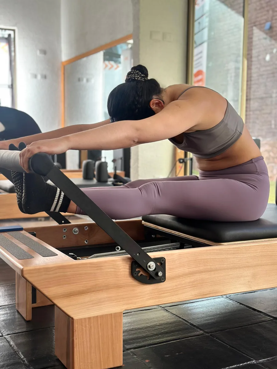 Alumna en estiramiento sobre Reformer con luz natural en el estudio