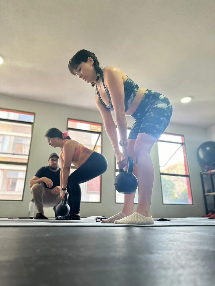 Alumna realizando deadlift con kettlebell junto a instructor